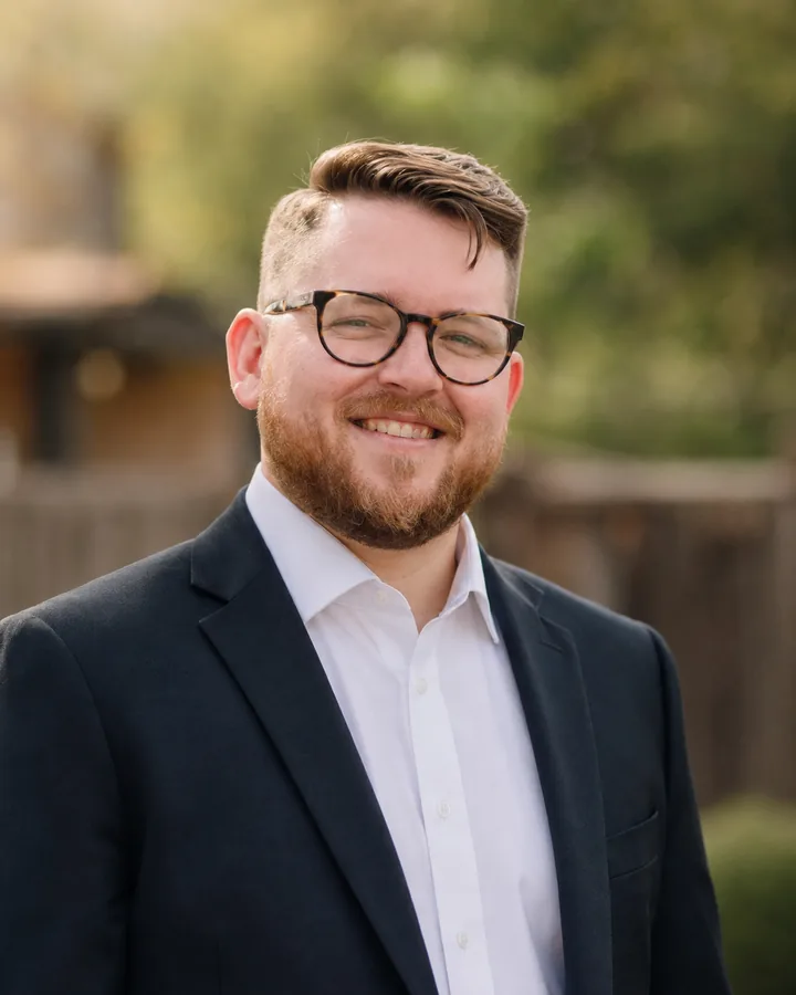 Erik Leavell smiling in tortoiseshell glasses, a navy blazer and an open-collar white shirt.